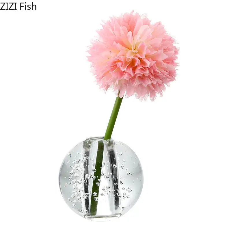 A delicate pink artificial carnation in a decorbites clear glass spherical clear glass vase with bubbles for desk decor