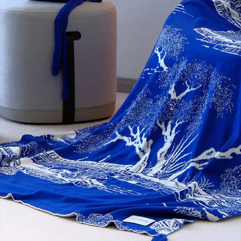 Royal blue and white knitted sofa blanket featuring a detailed landscape print and soft fringed edges for living room use