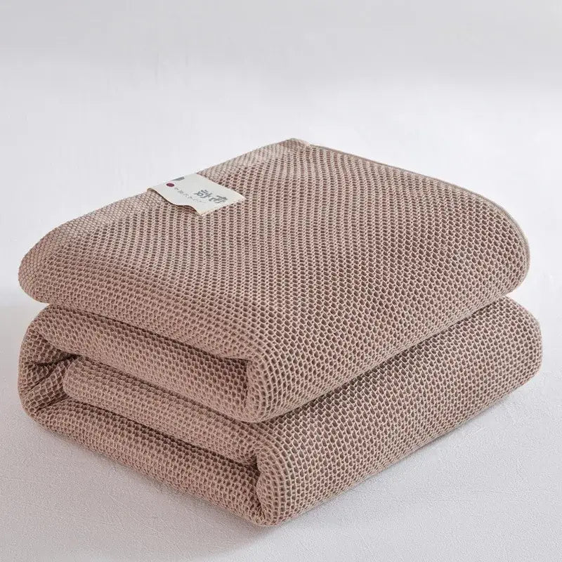 A neatly folded taupe decorbites cotton honeycomb towel blanket with textured mesh pattern for living room couch decor