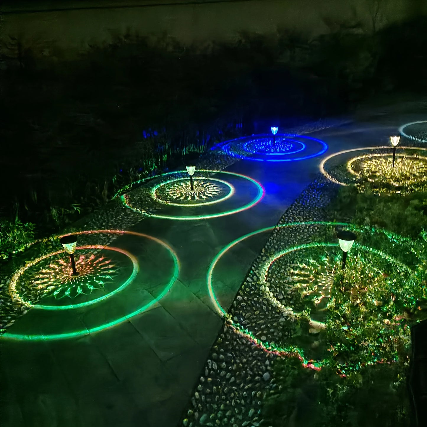 Colorful outdoor waterproof solar powered LED garden path lights casting green blue and yellow circular radiant patterns