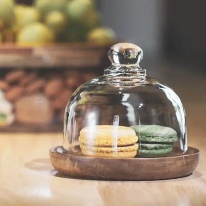 A clear glass dome with a silver knob on a dark wooden base for 3 tier glass food storage containers