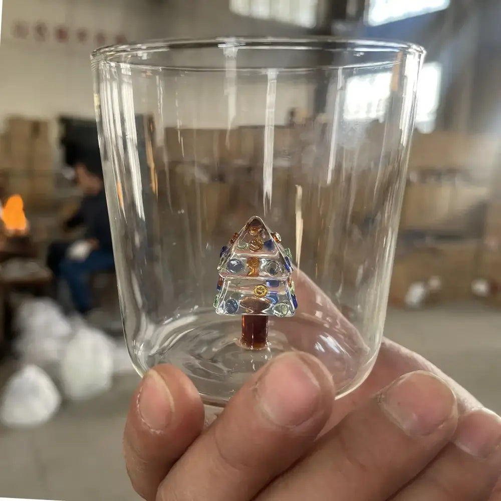 A clear glass 300ml 3d christmas tree wine glass with a colorful miniature christmas tree ornament inside