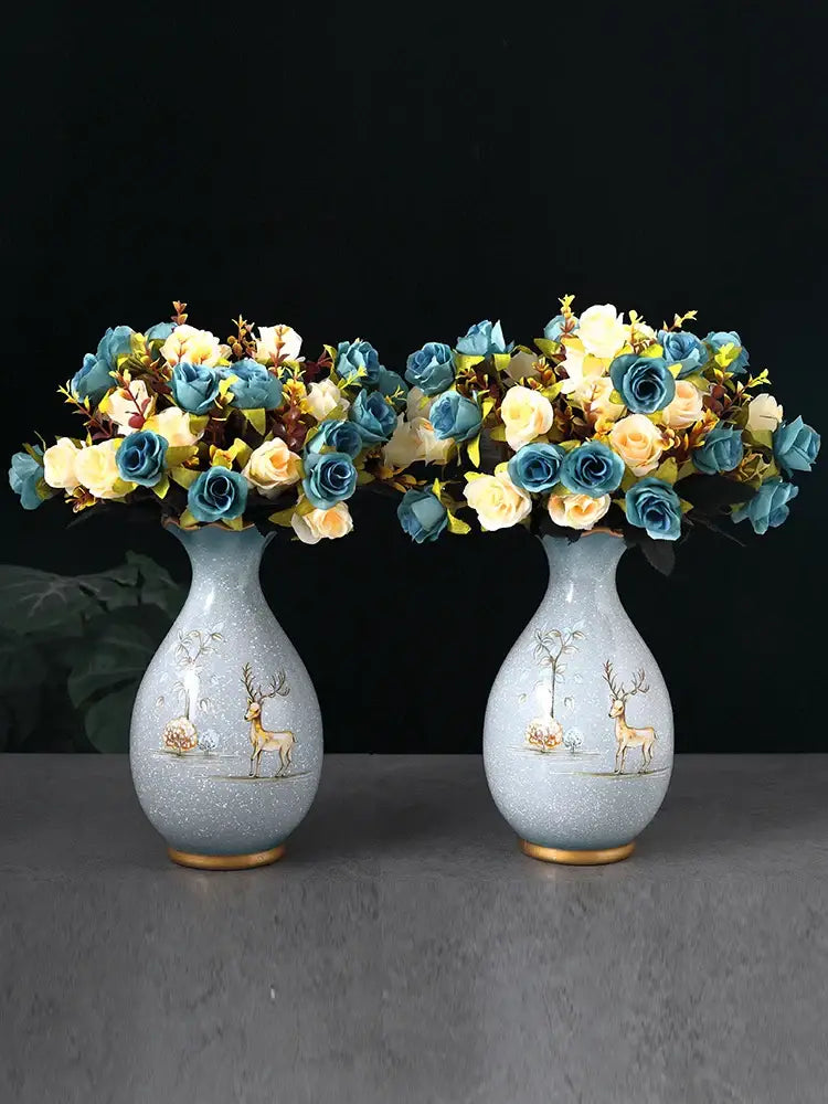 Pair of light blue ceramic vases with gold-trimmed deer design holding artificial blue and cream roses for dried flowers