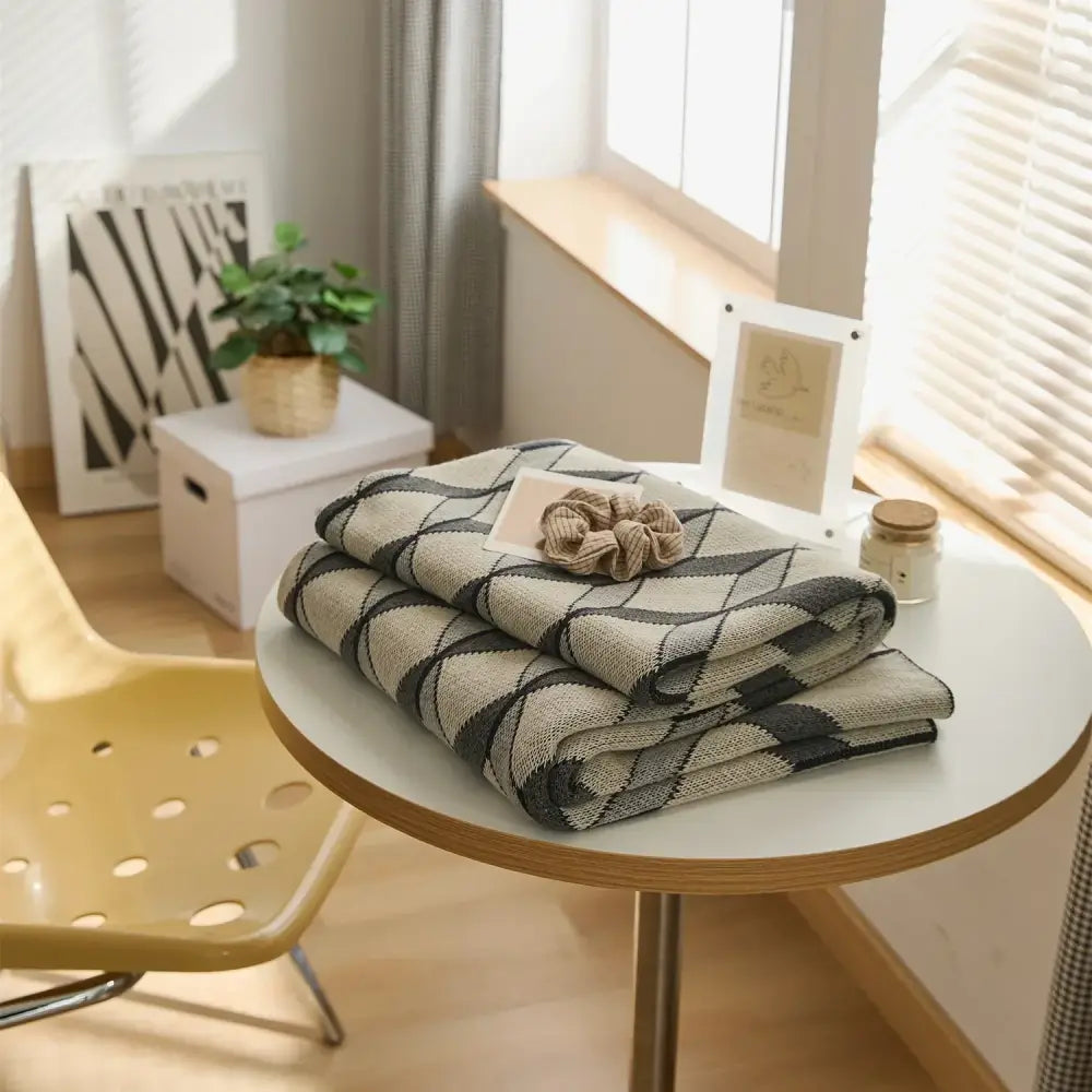 Folded gray and beige argyle patterned cube cotton knitted plaid blanket on white table decorbites 3d cube bedroom throw