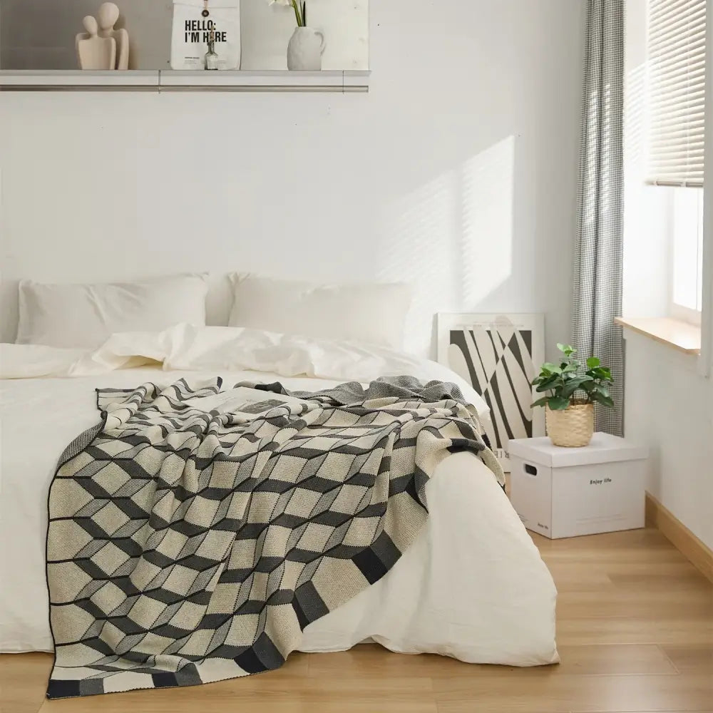 A cozy plaid blanket with black and beige geometric diamond pattern made from cube cotton knitted fabric draped on a bed