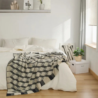 A cozy plaid blanket with black and beige geometric diamond pattern made from cube cotton knitted fabric draped on a bed