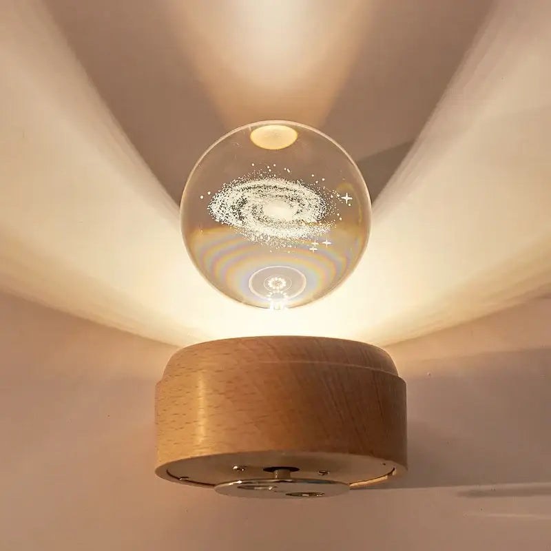 A clear glass decorbites crystal ball with a galaxy design mounted on a light wooden base night light and music box