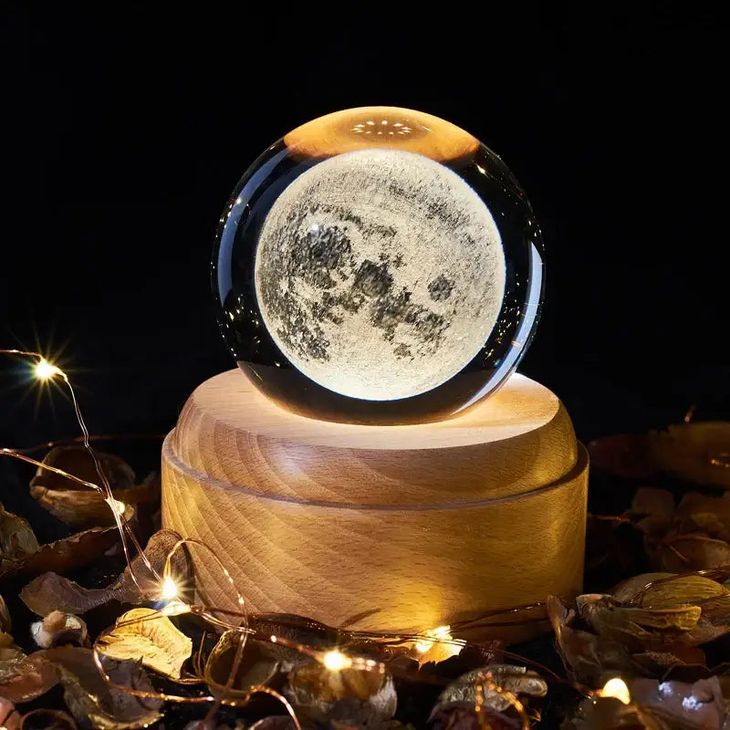 A clear glass decorbites crystal ball night light with illuminated moon on a wooden base for bedroom decor