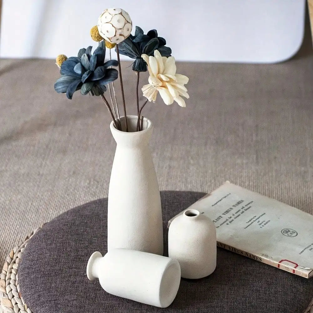White ceramic vase with slender neck and rounded body holding blue cream and yellow dried flowers in bohemian set