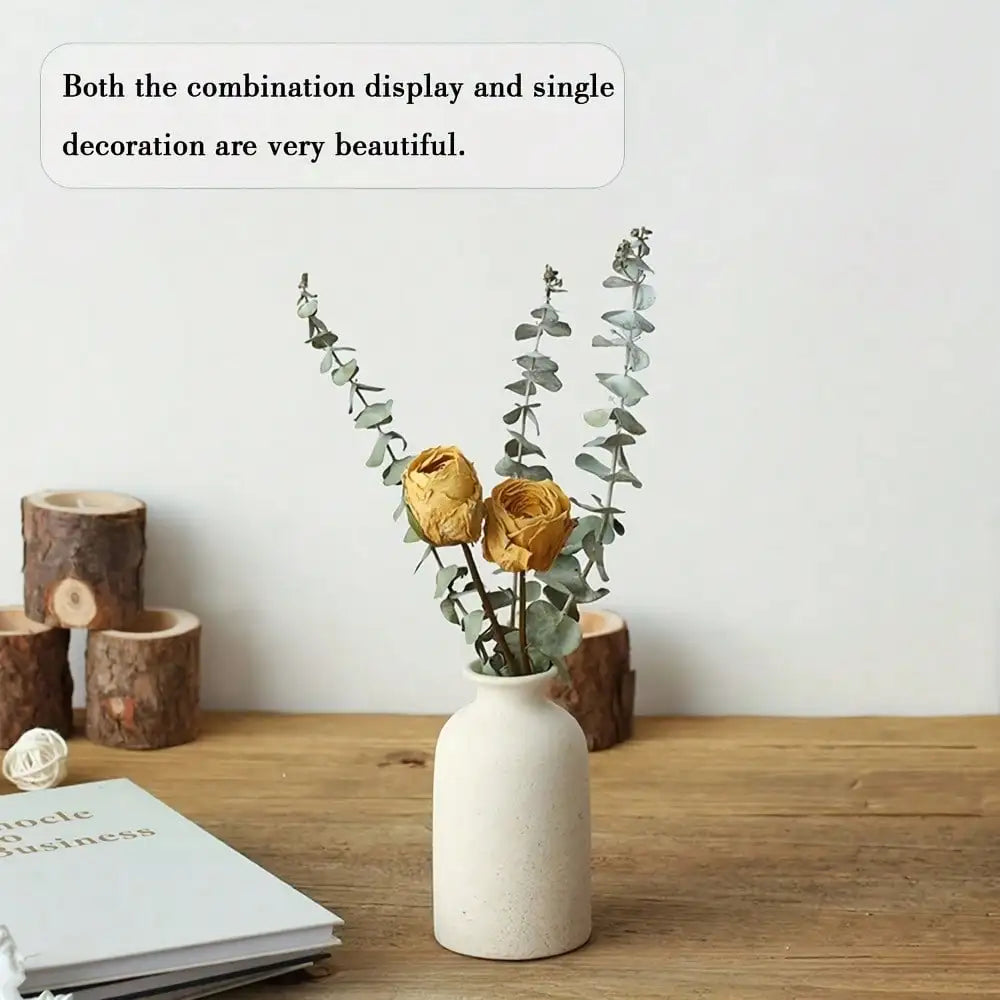 Minimalist white ceramic vase with two dried golden roses and eucalyptus branches in bohemian home decor setting