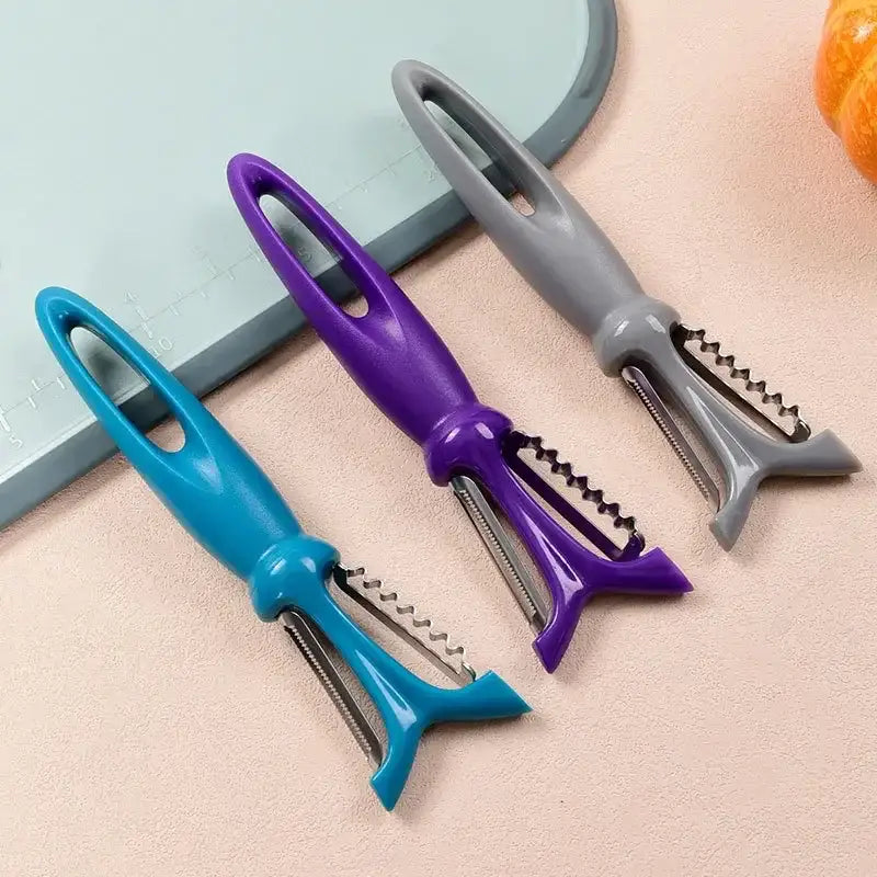 Three colorful plastic-handled stainless steel vegetable peelers with teal purple and gray handles for kitchen use