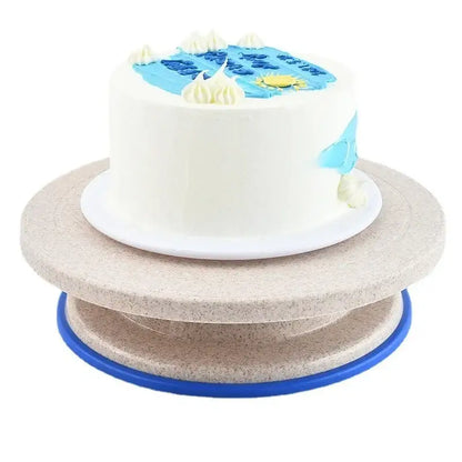 A white frosted cake with blue and yellow icing on a beige multi-tiered decorbites cake decorating turntable stand