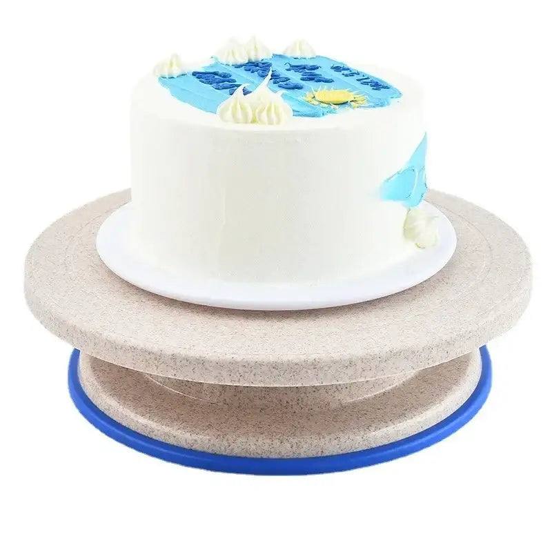 A white frosted cake with blue and yellow icing on a beige multi-tiered decorbites cake decorating turntable stand