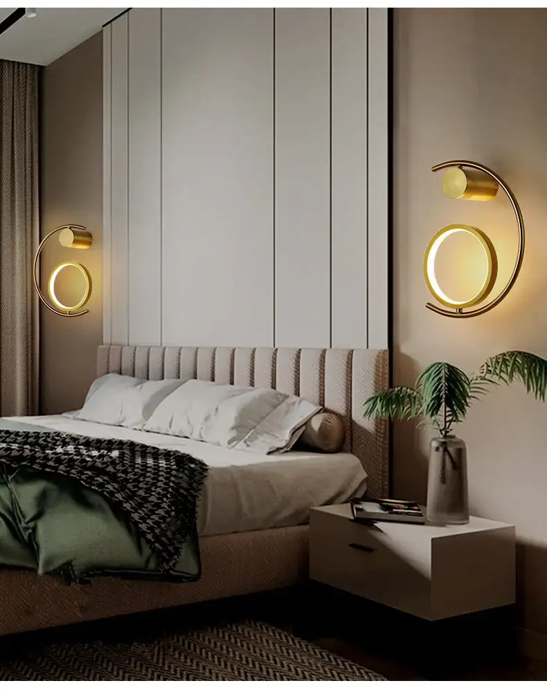 Gold-toned circular wall sconces with a modern minimalist design for a luxury creative led bedside wall lamp in the bedroom.