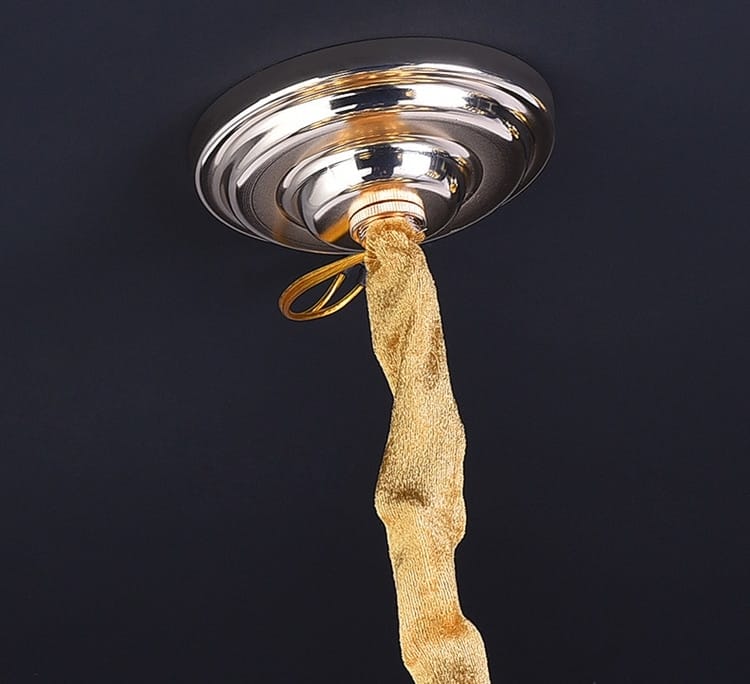 A polished chrome ceiling fixture with a textured gold fabric cord hanging from a luxury k9 crystal tiered chandelier for dining room lighting by Nebra luxury.
