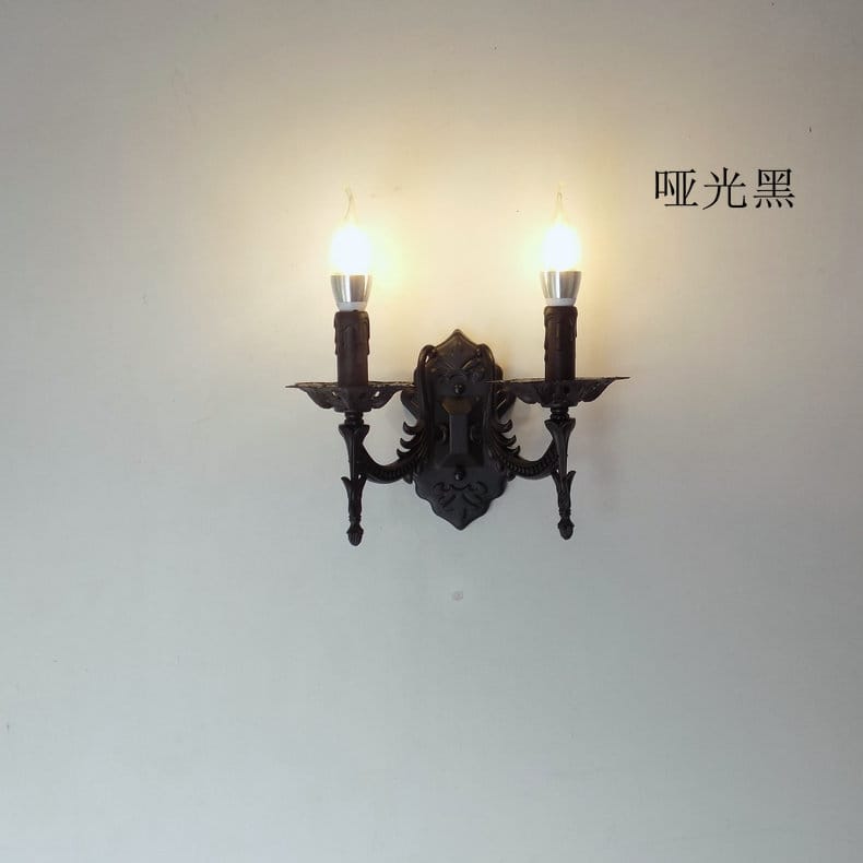 Matte black wrought iron two-light wall sconce with ornate candle-style arms and decorative central motif for creative retro european bedroom lighting.