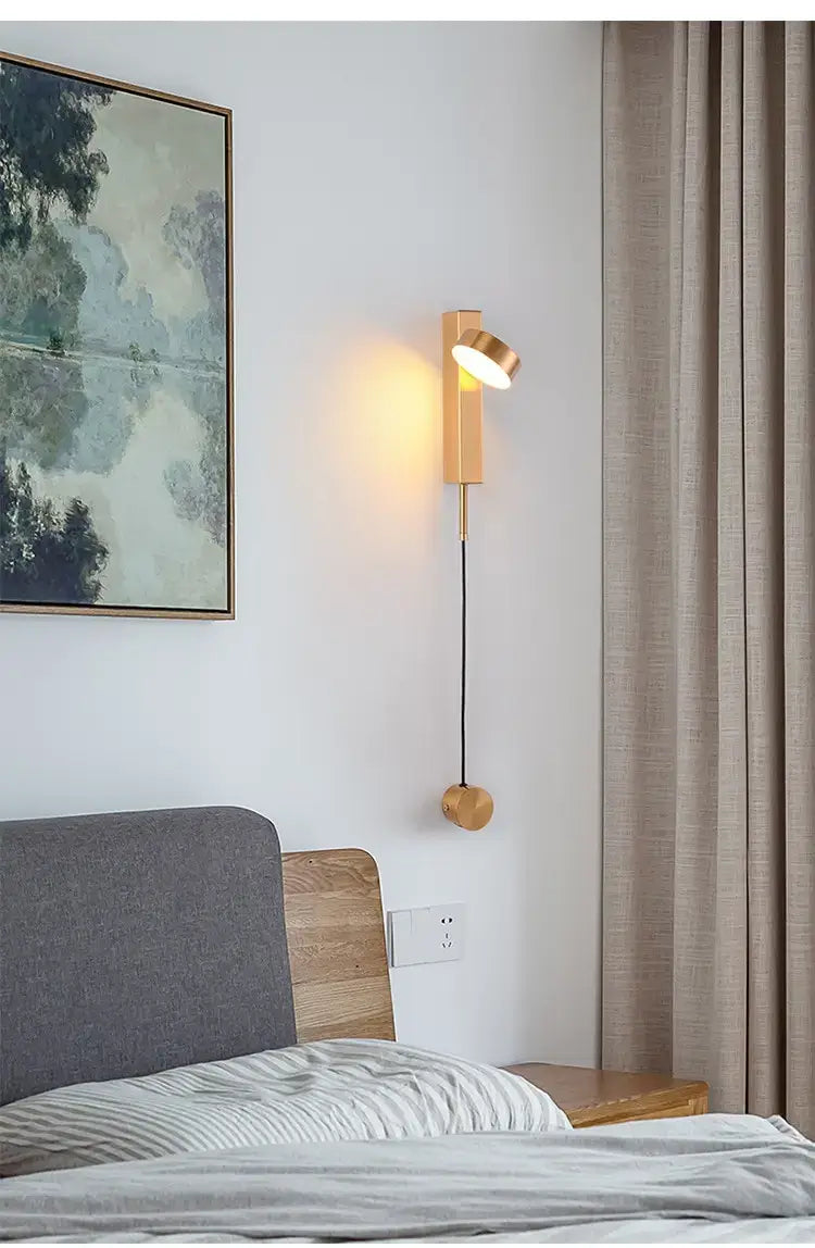A modern gold led wall lamp featuring a brass cylindrical body, adjustable spotlight head, and spherical base designed for bedroom use as a rotating led wall lamp.
