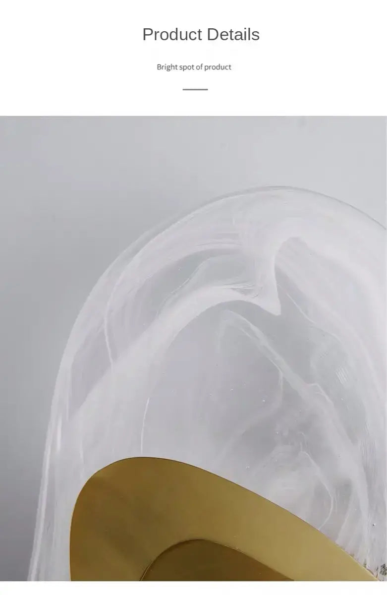 A modern creative minimalist glass wall lamp featuring a translucent white sculptural form with smooth curves and a contrasting gold circular base for bedroom bedside lighting.