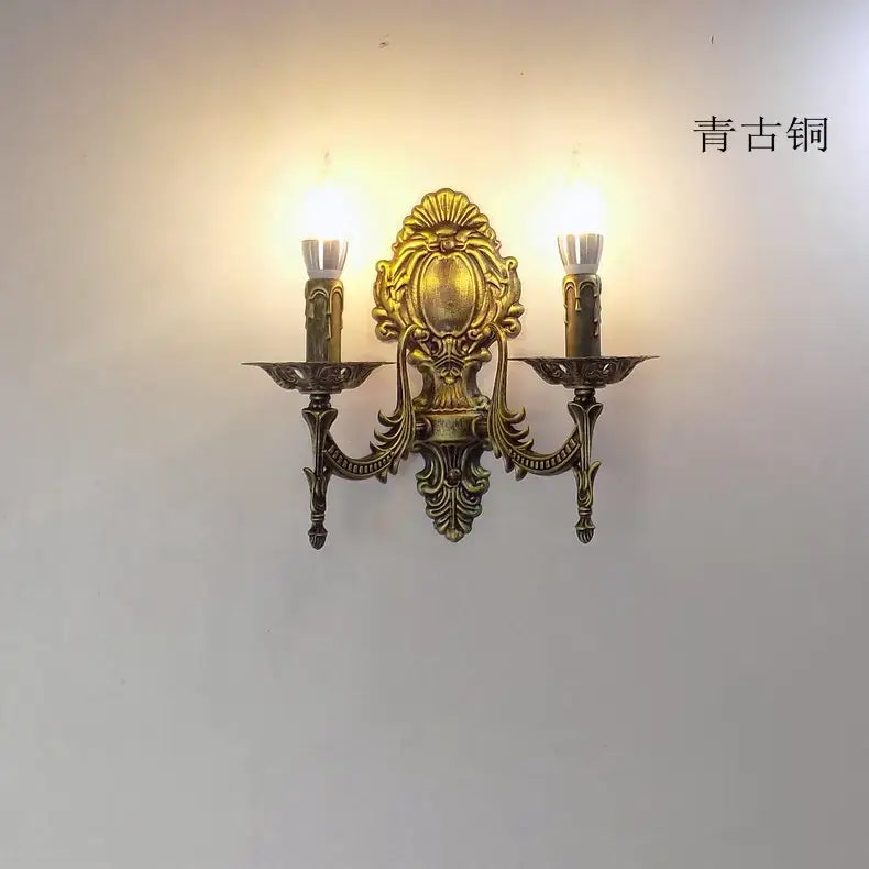 Antique brass two-light european wall light with ornate scrolled design and candle-style bulbs in creative retro european style for bedroom use.
