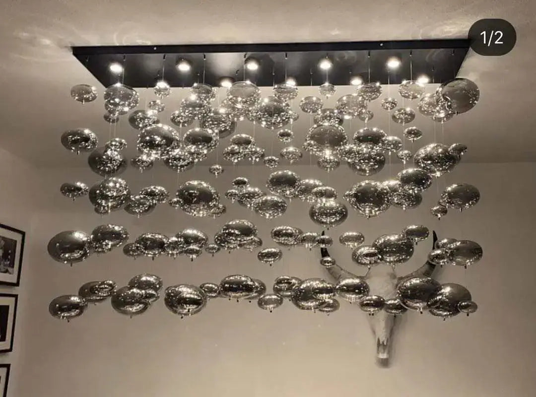A modern oval bubble ball silver chandelier dining room light fixture with numerous reflective silver-toned spherical glass orbs suspended from a sleek black rectangular frame.