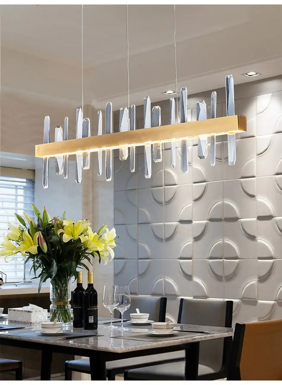 Modern rectangle gold crystal chandelier featuring linear pendant light with clear crystal-like vertical accents hanging above a dining table.