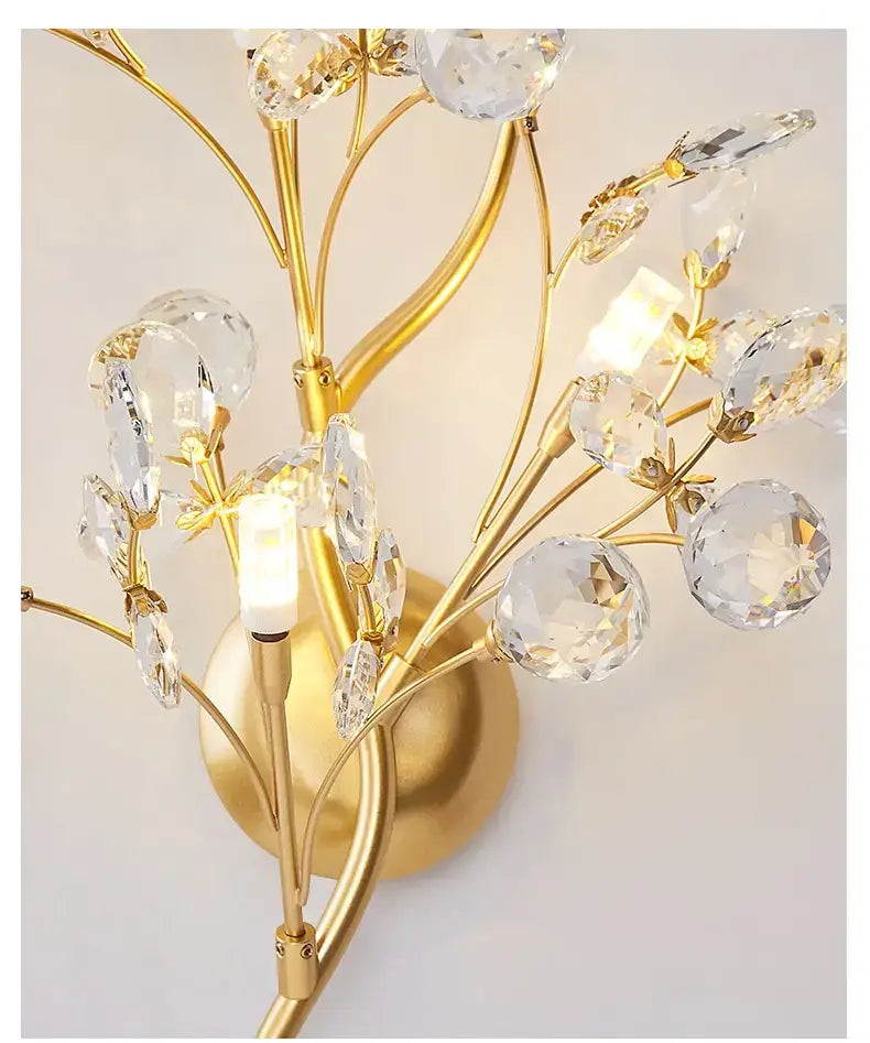post modern luxury gold-toned wall sconce featuring crystal embellishments shaped like blossoms and leaves in a luxury branch style for bedroom lighting
