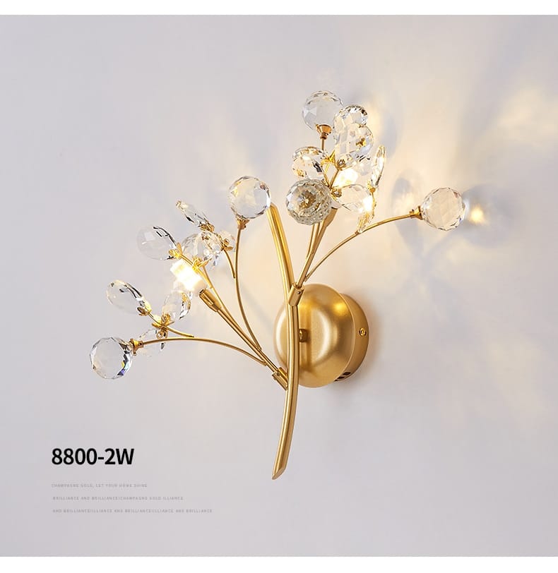 Gold-toned wall sconce with clear crystal spheres arranged in a branching floral design for post modern luxury bedroom lighting in modern luxury branch style.