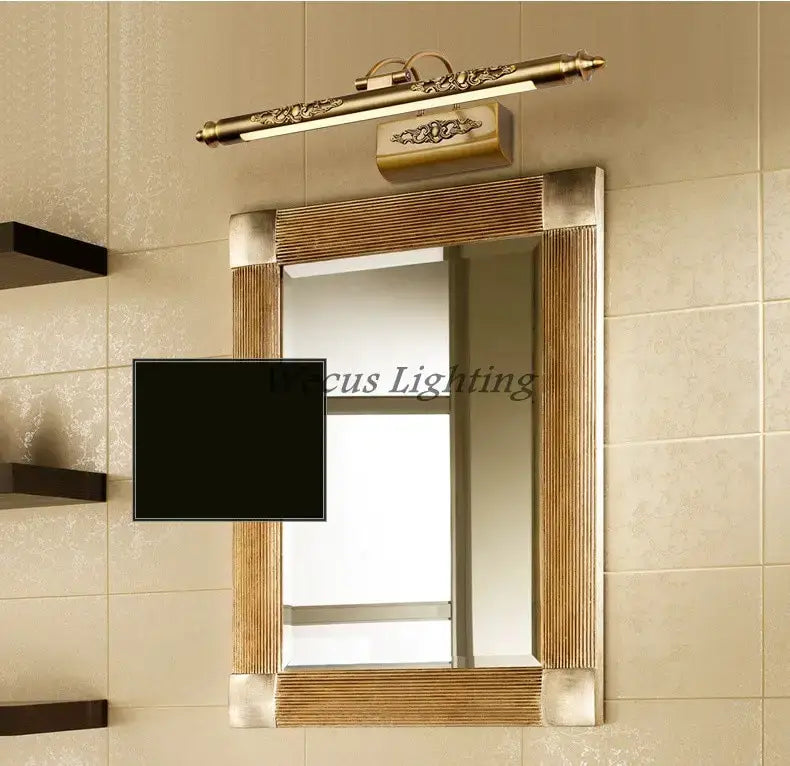 antique bronze ornate led mirror lamp with brass-finished wall-mounted vanity light above a rectangular mirror with ribbed wooden frame and metallic corners for bathroom wall decor.