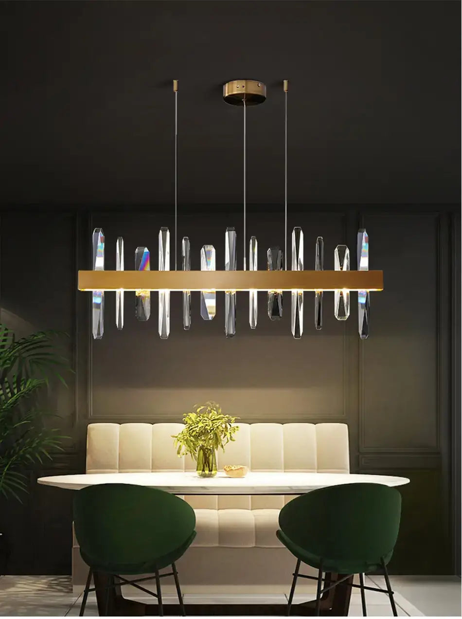 Modern rectangle gold crystal chandelier with clear crystal-like pendant elements suspended from a central bar for dining room lighting.