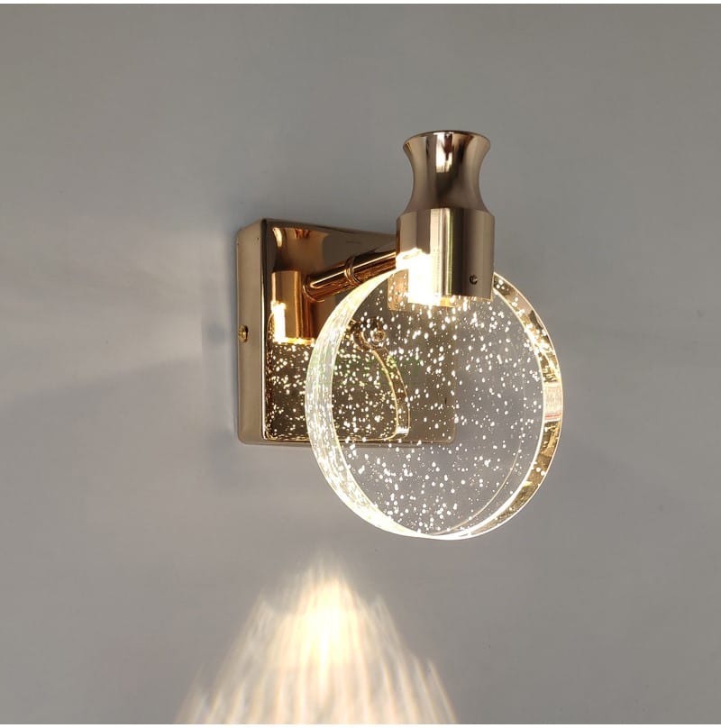 A modern gold-toned simple crystal led wall lamp featuring a clear circular glass globe filled with sparkling particles designed for bathroom lighting.