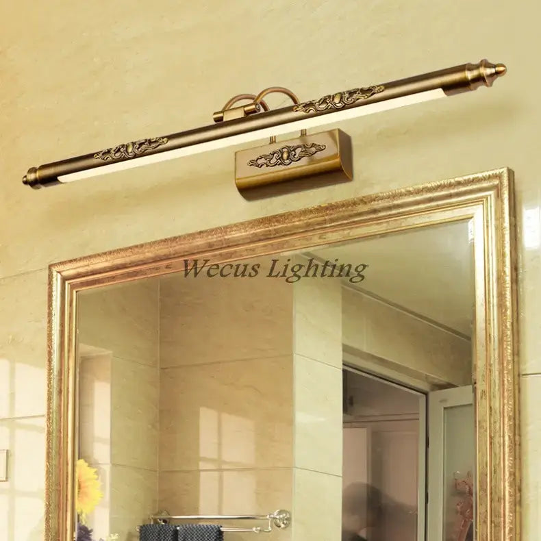 Antique bronze ornate led mirror lamp with brass finish and scrollwork detailing on rectangular fixture housing for bathroom wall decor.