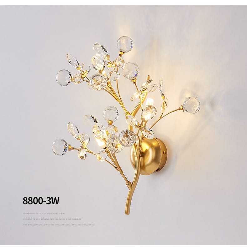 Post modern luxury gold crystal branch wall sconce designed as a gold-toned flowering branch with clear crystal-like beads and bulbs for modern luxury branch style lighting.
