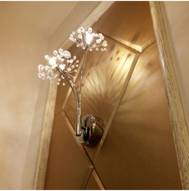 chrome-finished nordic creative crystal wall lamp with two branching arms adorned with clear crystal beads resembling dandelion seed heads designed for bedroom use.
