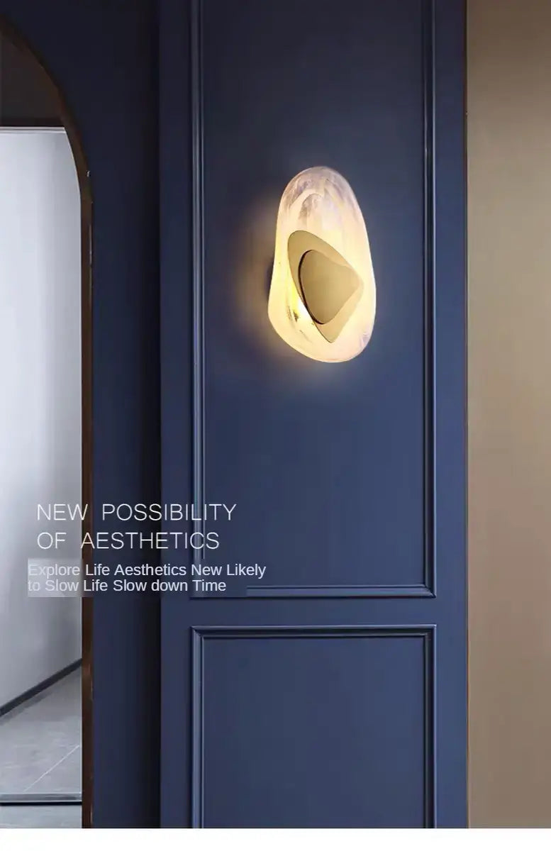 Modern creative minimalist glass wall lamp with a warm glowing light in an organic shell-like form made of polished stone or resin for bedroom bedside lighting.