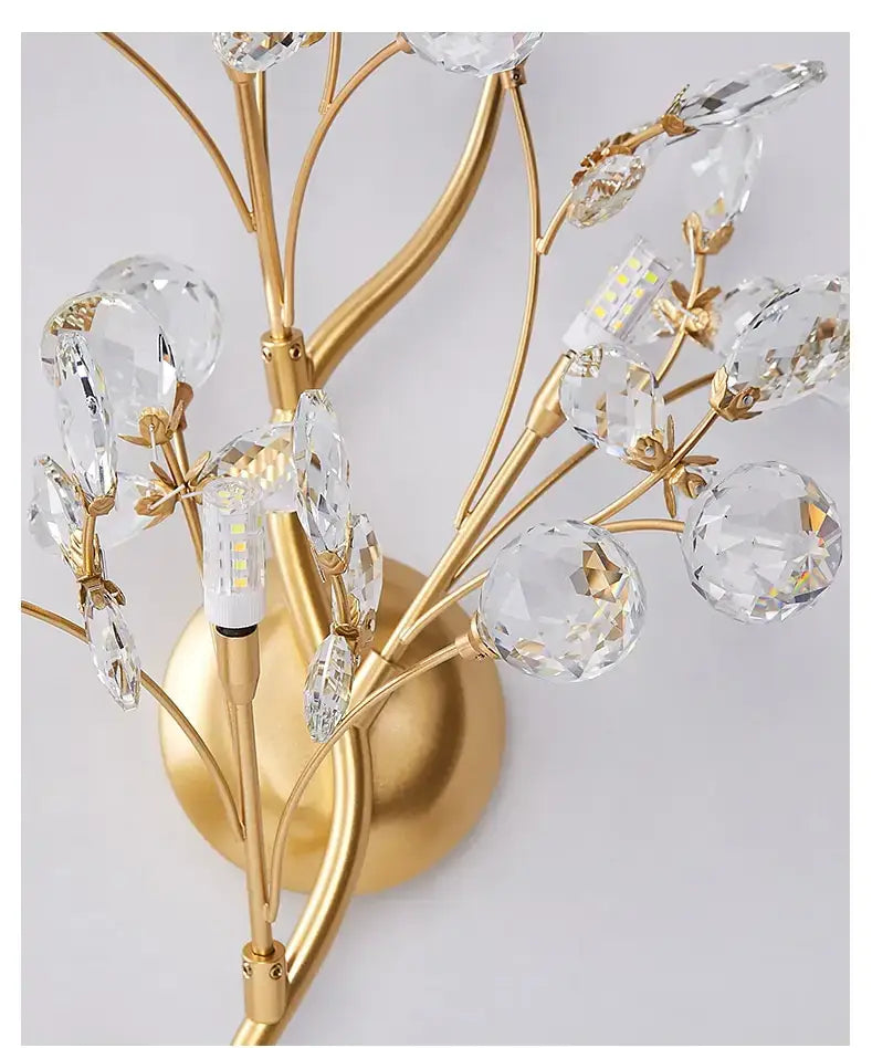 Post modern luxury gold crystal branch wall sconce features gold-toned branching arms with clear faceted crystal orbs and leaf-like accents designed for elegant bedroom lighting.