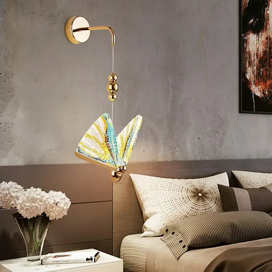 A gold-toned wall light featuring a butterfly led wall shade with intricate yellow, green, and white mosaic patterns designed for bedroom use.