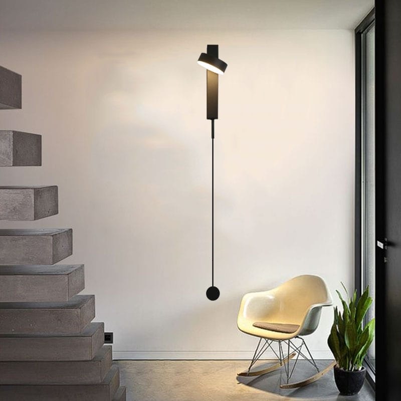 Black minimalist wall lamps with a sleek elongated vertical stem and circular base featuring a rotating modern led wall sconce light for bedroom use.