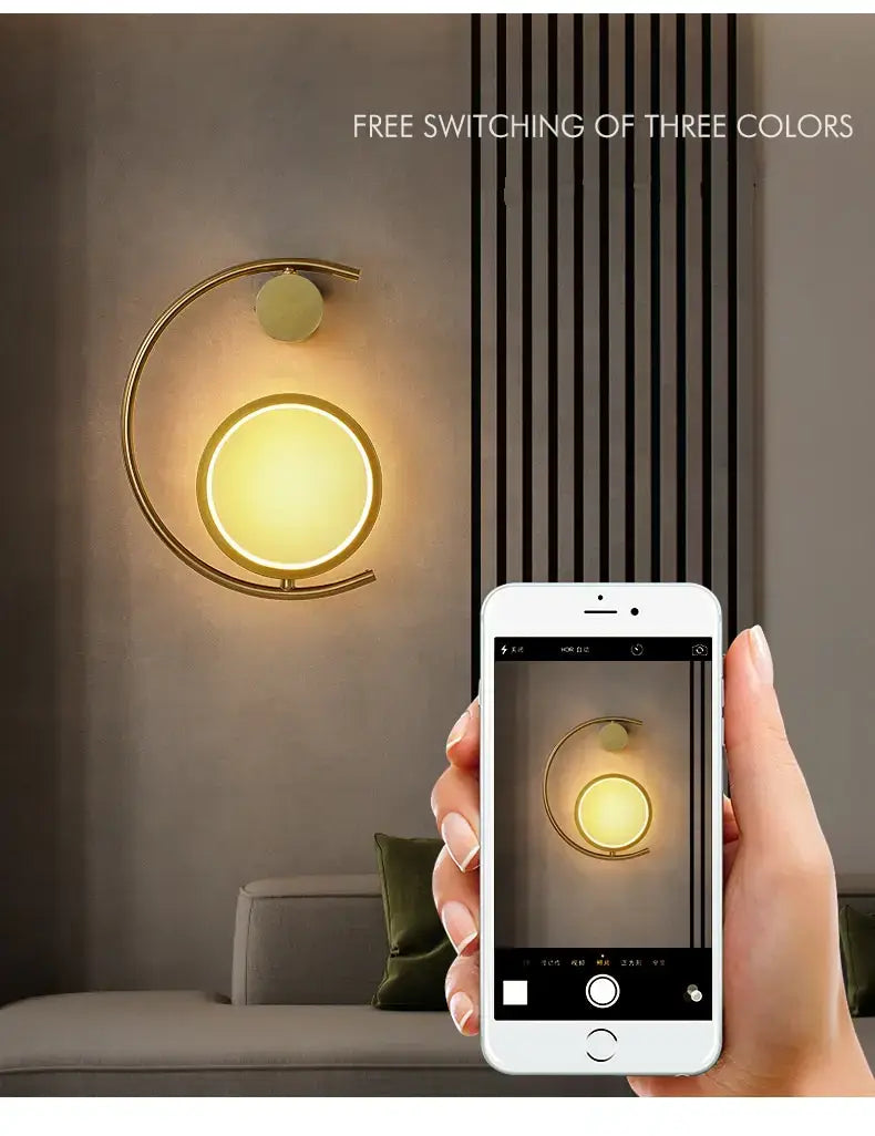 Modern gold luxury creative led bedside wall lamp featuring a circular illuminated face with free color switching and a curved metallic frame designed for bedroom use.