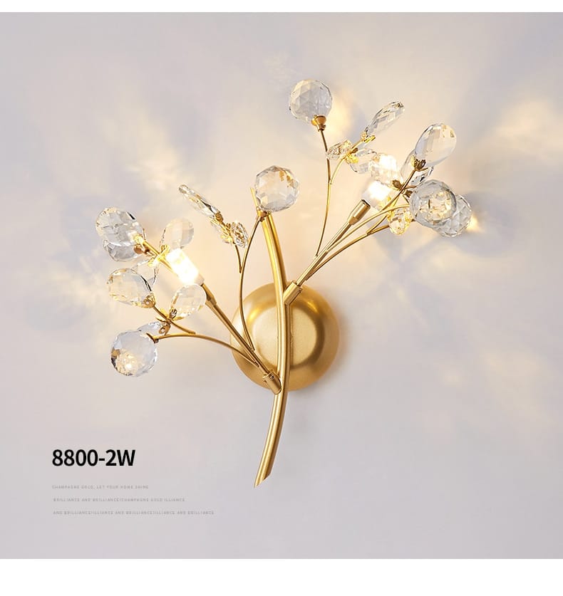 Gold-toned post modern luxury wall sconce with delicate branch-like arms adorned with clear crystal beads and teardrop-shaped crystals ideal for bedroom lighting in luxury branch style.