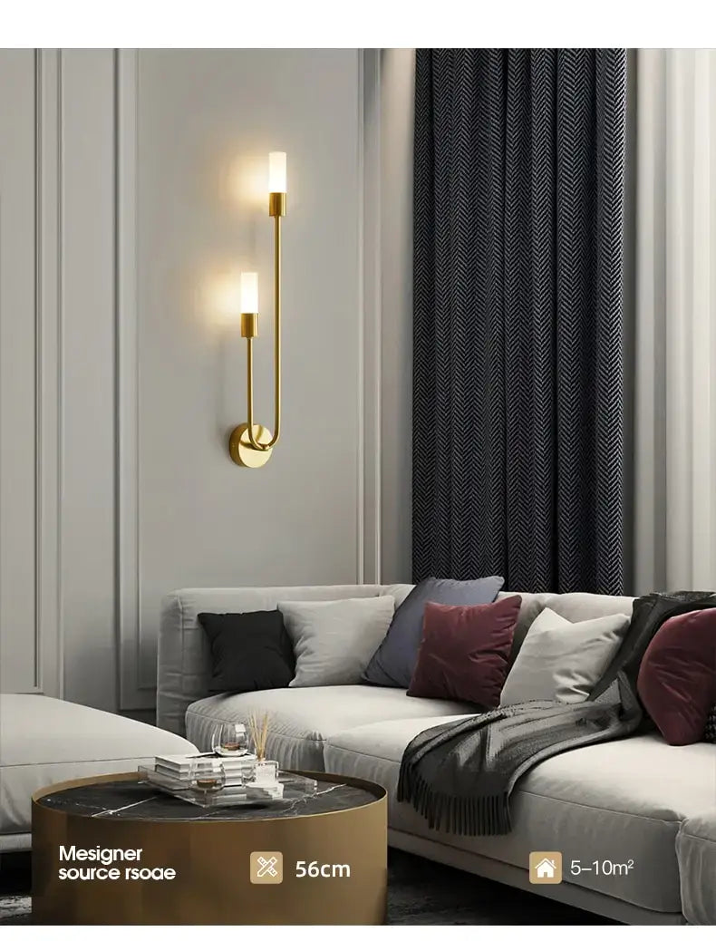 Modern gold-tone wall lamp with two vertical candle-style led lights and a sleek curved design ideal for bedroom use.