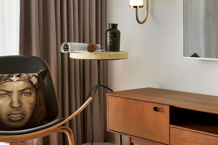 black cushion featuring a detailed portrait with intricate floral and headband patterns placed beside a modern minimalist gold led wall lamp cylindrical sconce for bedroom use.