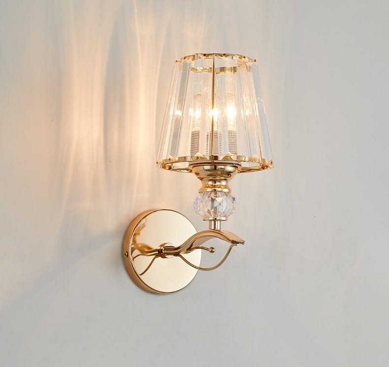 modern minimalist wall sconce in gold tone featuring a faceted crystal shade and decorative curved arm for bedroom lighting.