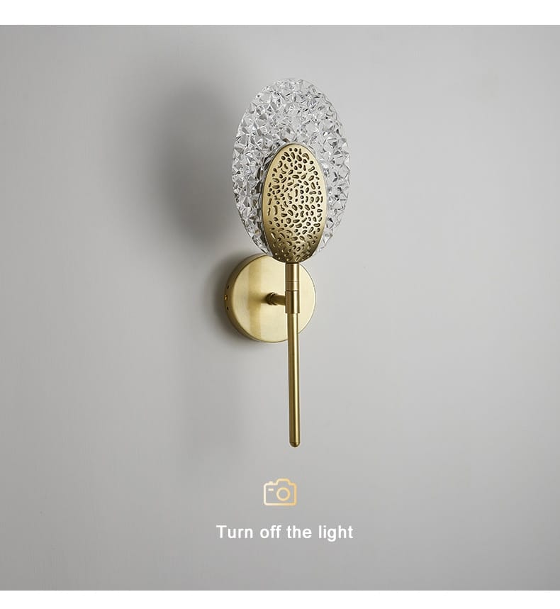 Gold-toned led wall lamp with a textured oval metal shade and a faceted crystal disc designed for indoor lighting in the bedroom.
