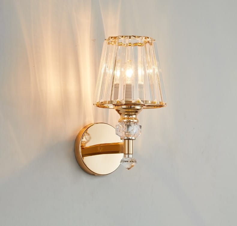 Modern minimalist wall lamp with gold finish and faceted crystal shade featuring decorative crystals for bedroom lighting.