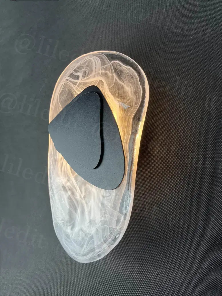 Transparent swirling resin slipper with a sleek black insole paired with a modern creative minimalist glass wall lamp for bedroom bedside lighting.
