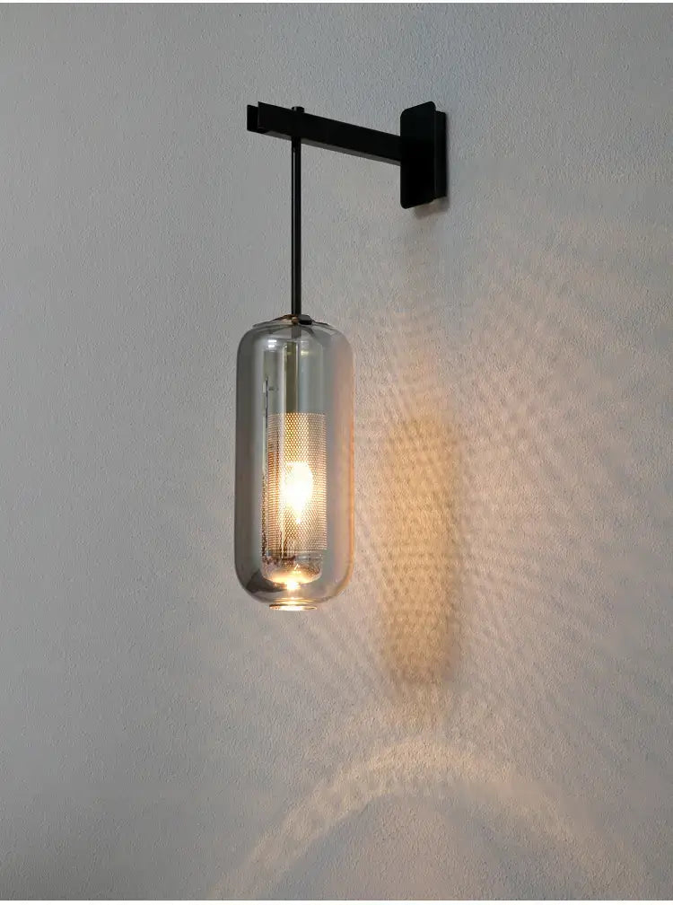 A sleek black metal nordic modern decor wall sconce featuring a cylindrical smoked glass lampshade with an illuminated bulb for modern decor glass lighting in the bedroom.