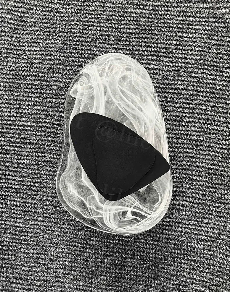 a black triangular guitar pick resting inside a translucent swirling glass container of a modern creative minimalist glass wall lamp for bedroom bedside lighting
