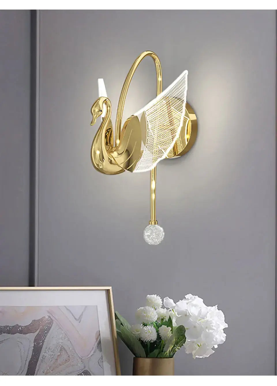 Art deco gold-toned swan wall lamp with a mesh wing and dangling crystal orb designed as a bedroom bedside wall lamp.