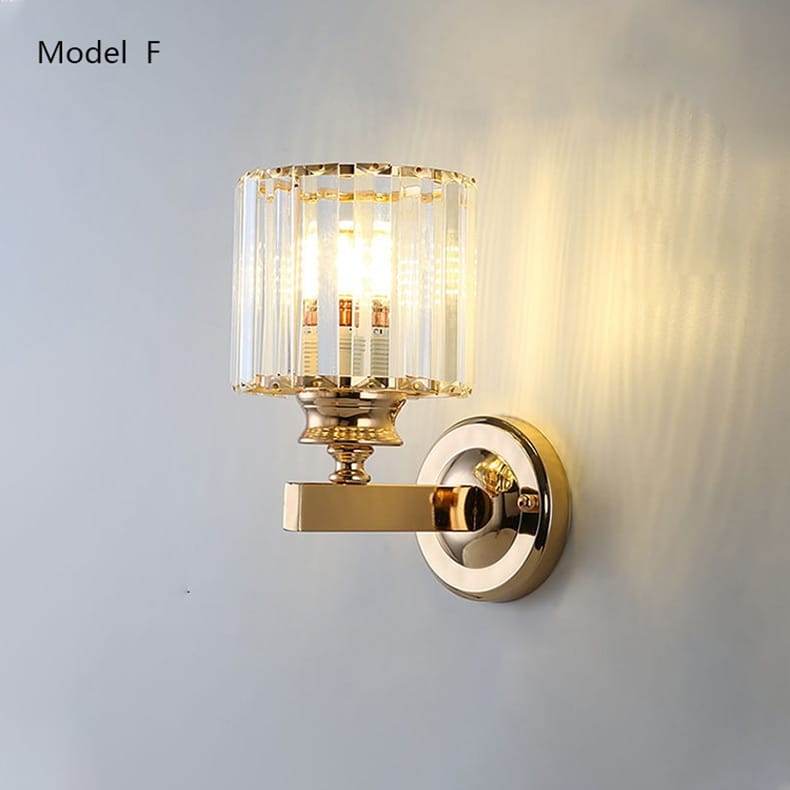 modern minimalist wall sconce in gold tone featuring a cylindrical crystal shade and polished brass accents designed for bedroom use