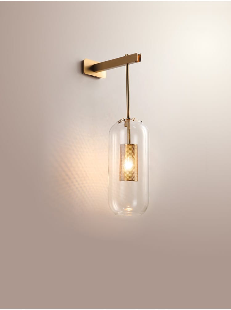 A modern brass wall sconce featuring a clear glass lampshade with a textured gold-finished bulb designed for nordic modern decor in the bedroom.